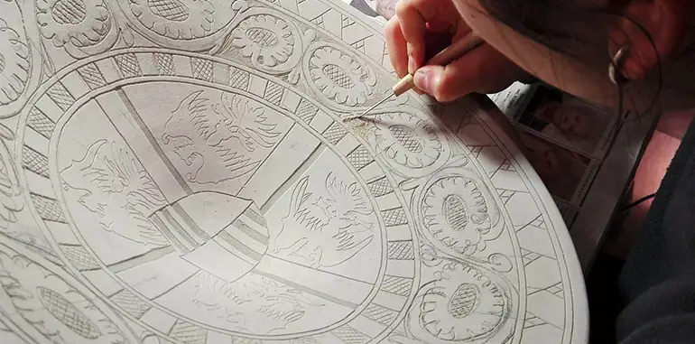 La Corte dei Gonzaga scratching a design on her ceramic wall plate. Then the artist will paint the plate and place it in the kiln for its final firing.