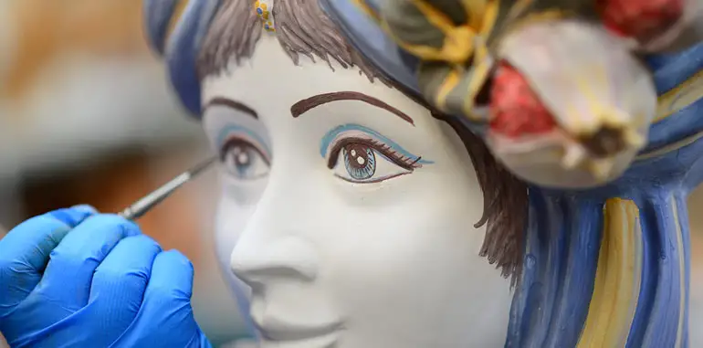 A Sicilian artist painting the eye of a large ceramic Moorish female head 